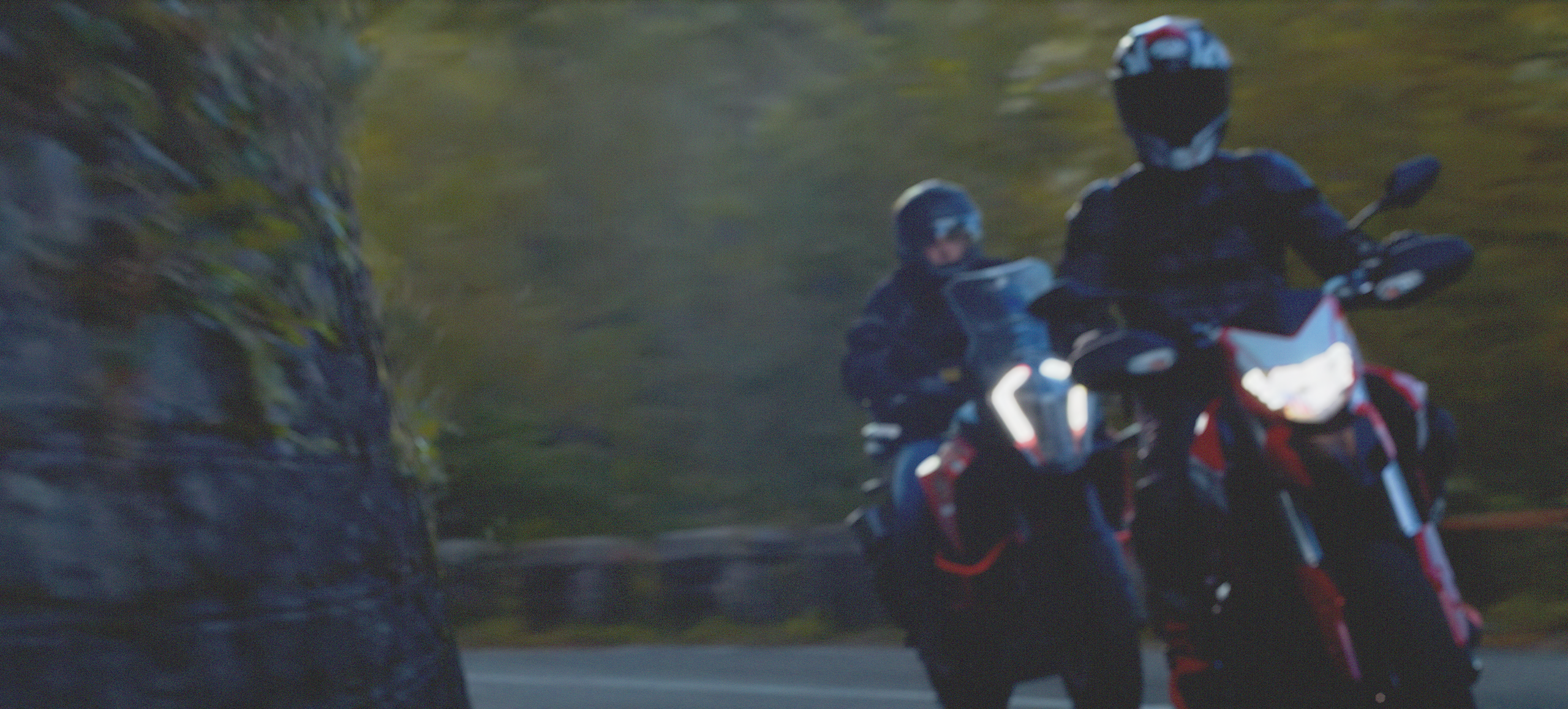 Two motorcyclists riding through a bend at dusk